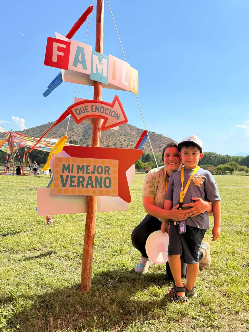 Mamá e hijo abrazados en el Campamento Mini Yoguis, junto al letrero Familia